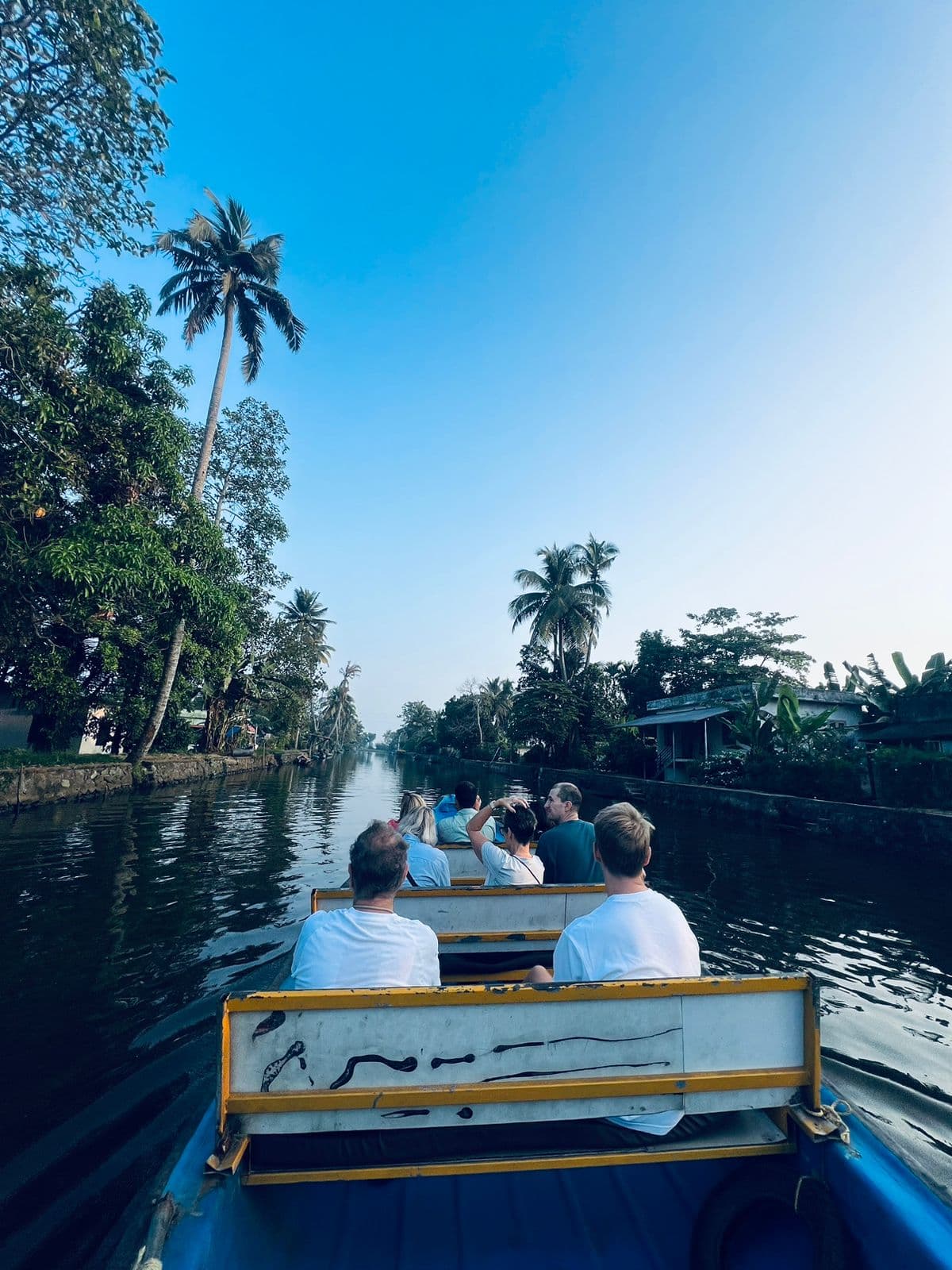 Guests riding along a calm daylight canal with a bridge and houses nearby