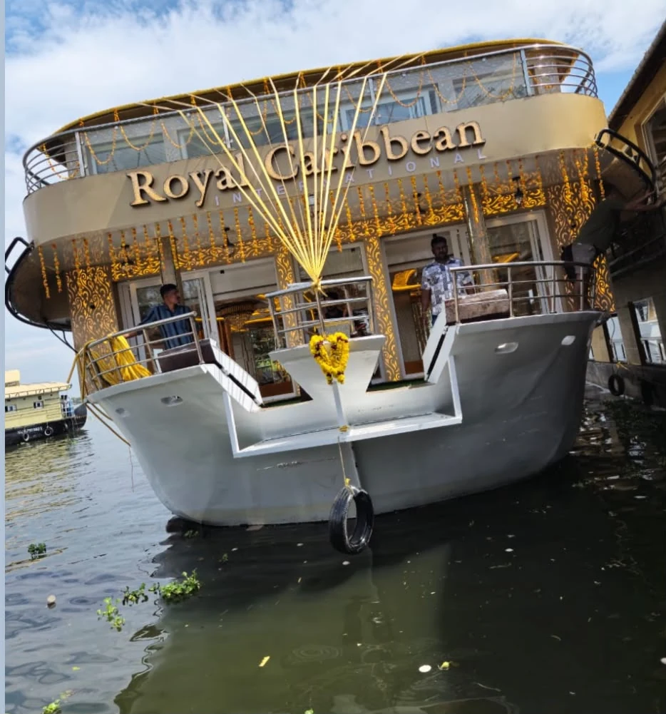 A houseboat at the jetty on the Alleppey backwaters, its bow hung with marigold garlands and the upper deck trimmed with flowers