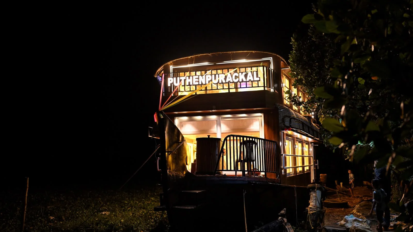 The three bedrooms Deluxe houseboat lit up at night, with a glowing name board on the upper deck