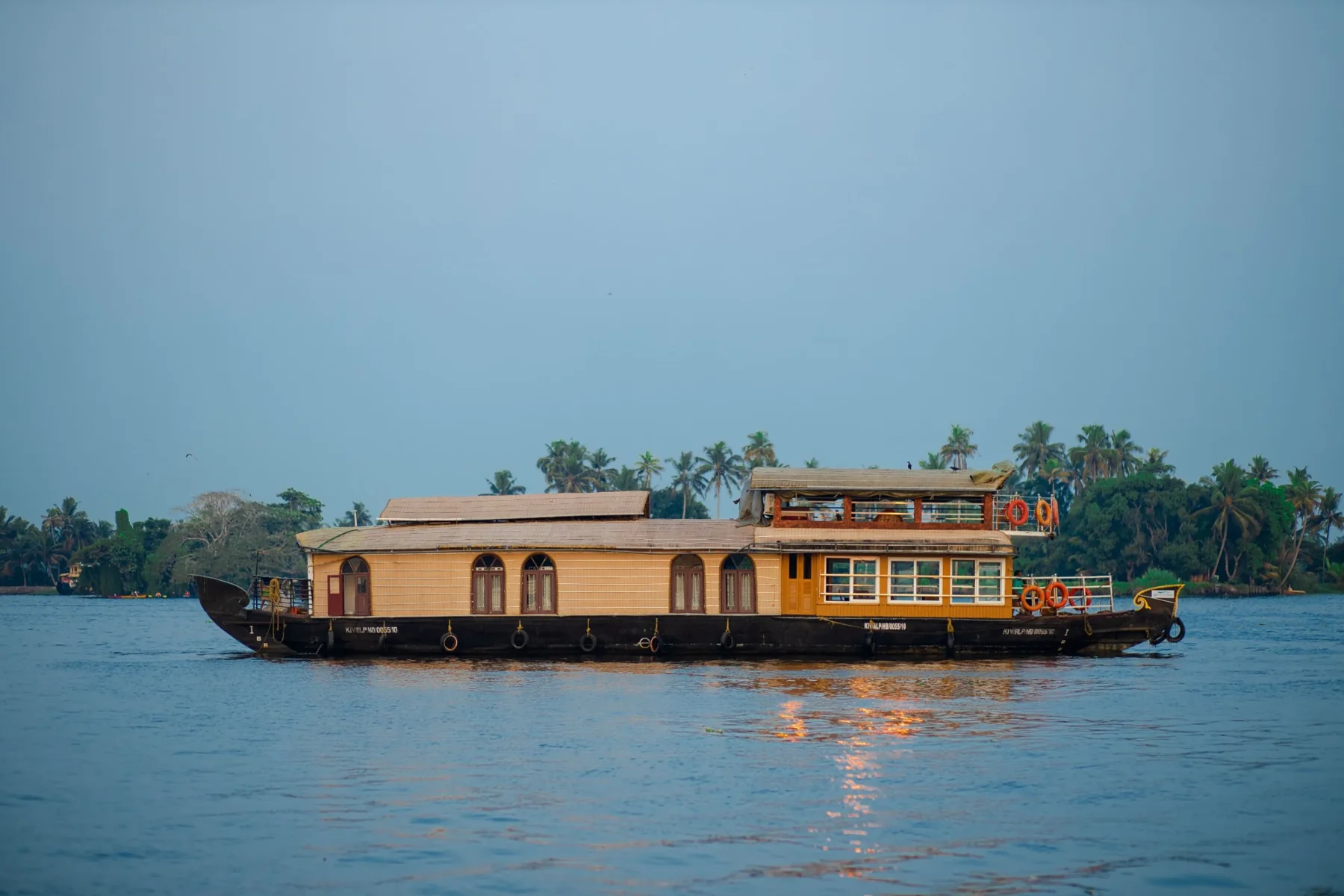 The two bedrooms Premium houseboat cruising across open water at dusk, with palms along the far bank