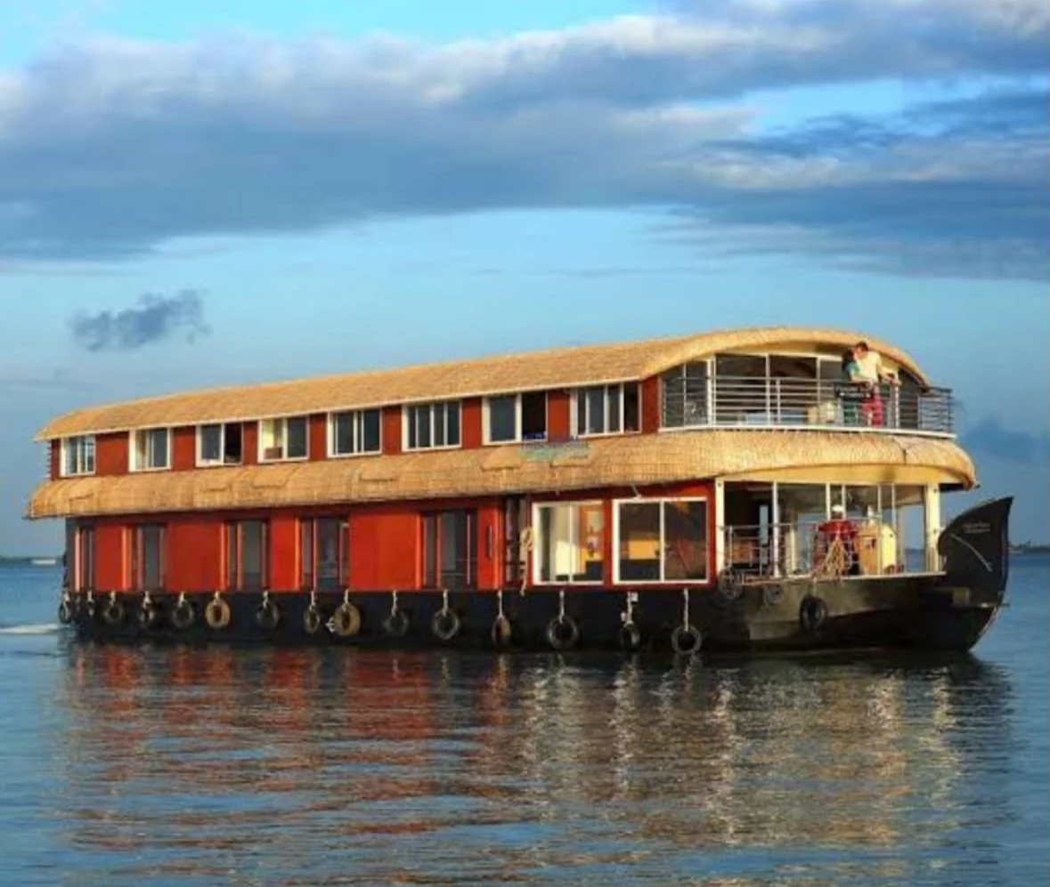 The six bedrooms Premium houseboat on open water at dusk, with a long red hull, thatched roofs and an open upper-deck lounge