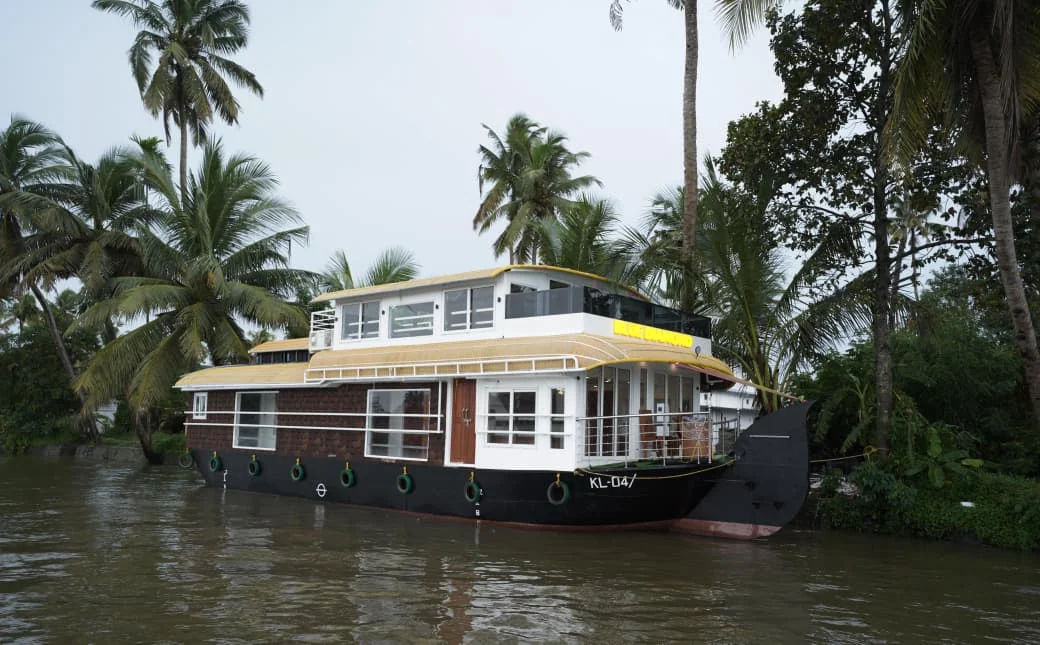 The two bedrooms Premium houseboat moored under coconut palms, with a glass-fronted upper deck