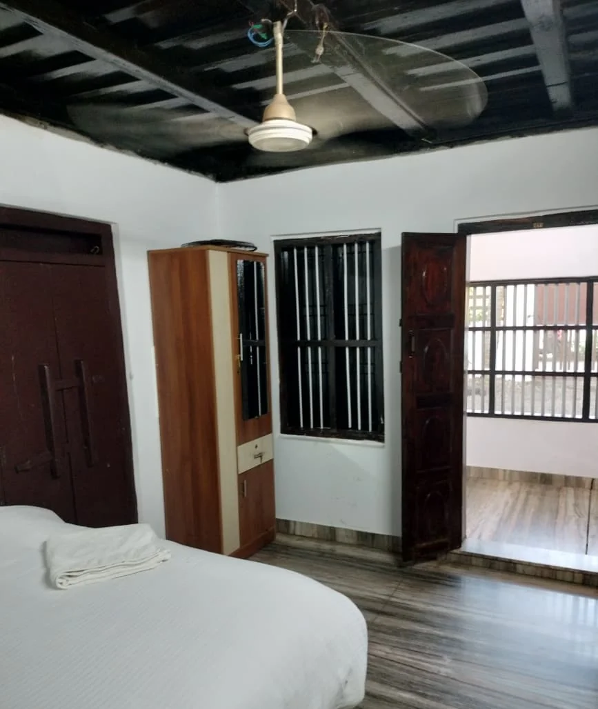 Spacious bedroom with a wardrobe, a barred window and a carved timber door onto the verandah