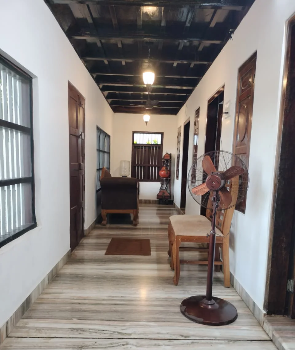 A long verandah with a polished stone floor, a carved sofa, doors with ornate panels and a dark timber ceiling