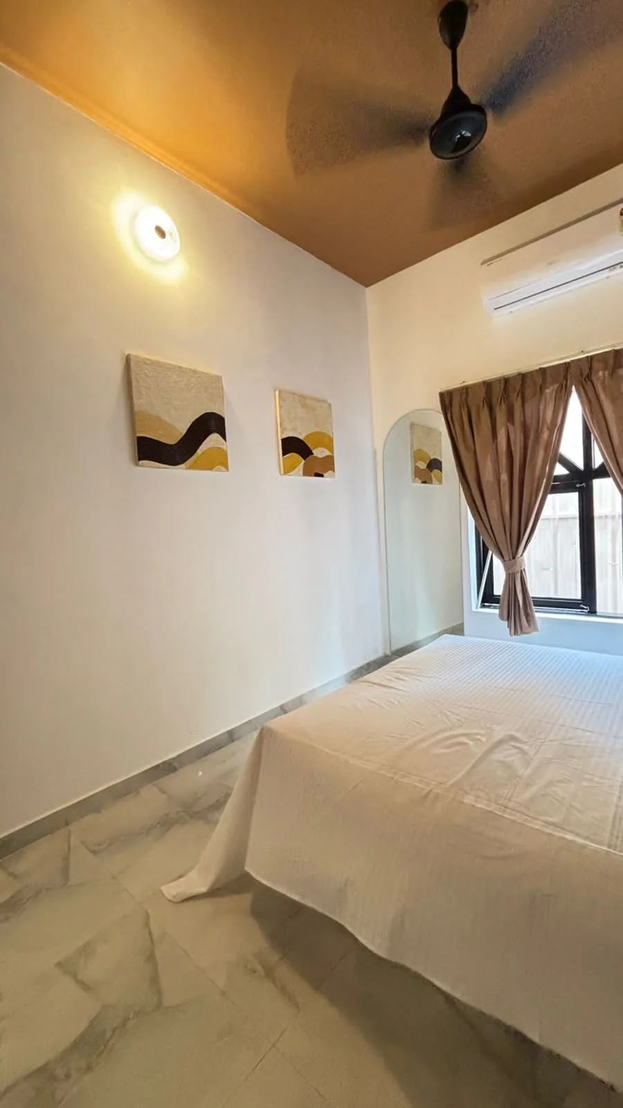 Bedroom with two abstract paintings, an arched mirror and curtained window beside the bed