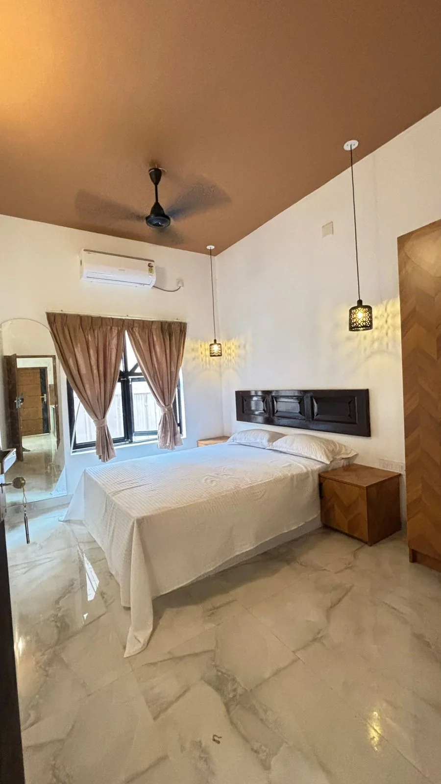 Bedroom with a white double bed, a carved dark headboard, pendant lamps and an arched mirror