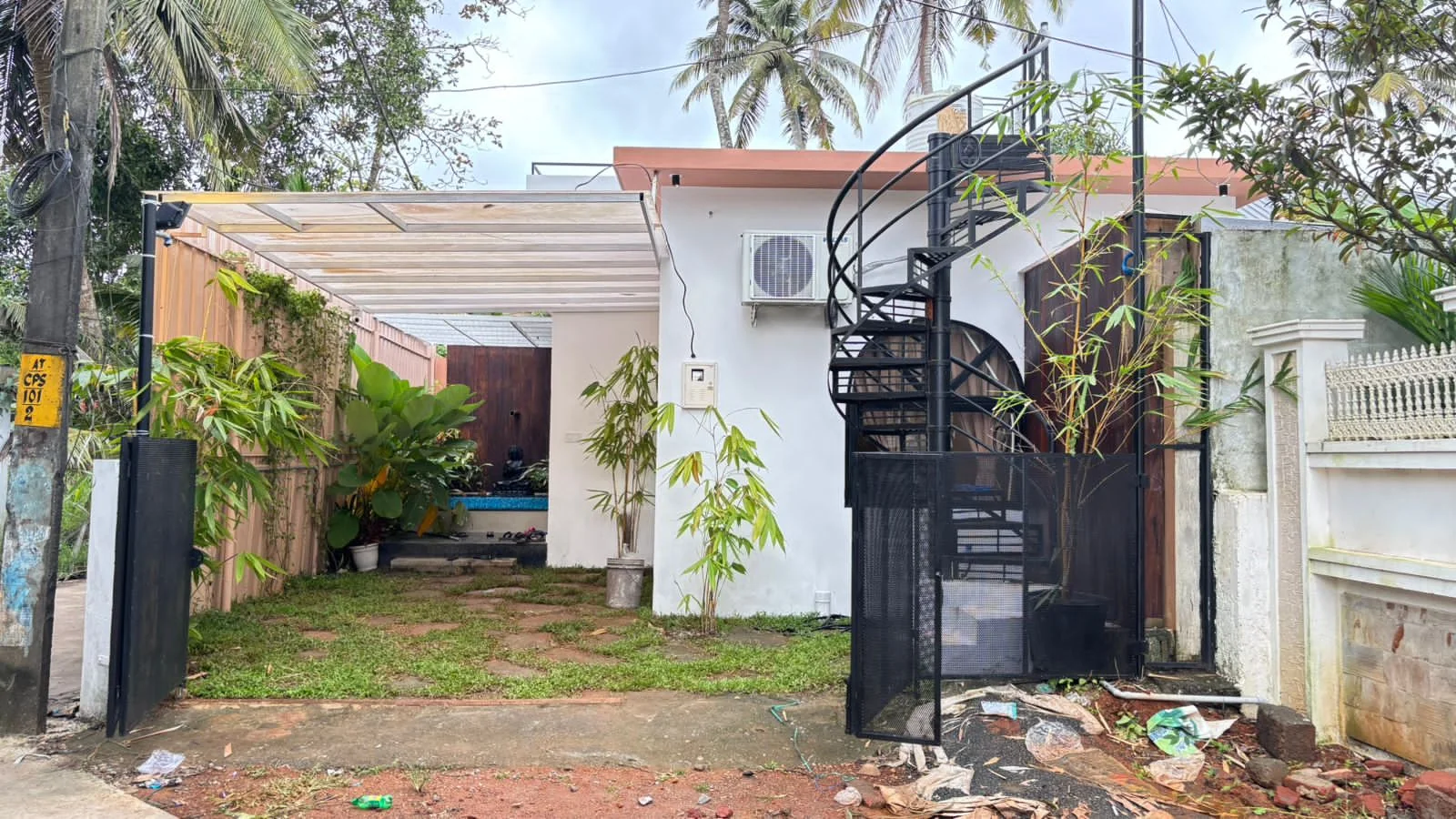 The pool villa from the gate: a white single-storey house with a spiral staircase to the roof and a pool courtyard behind a timber screen