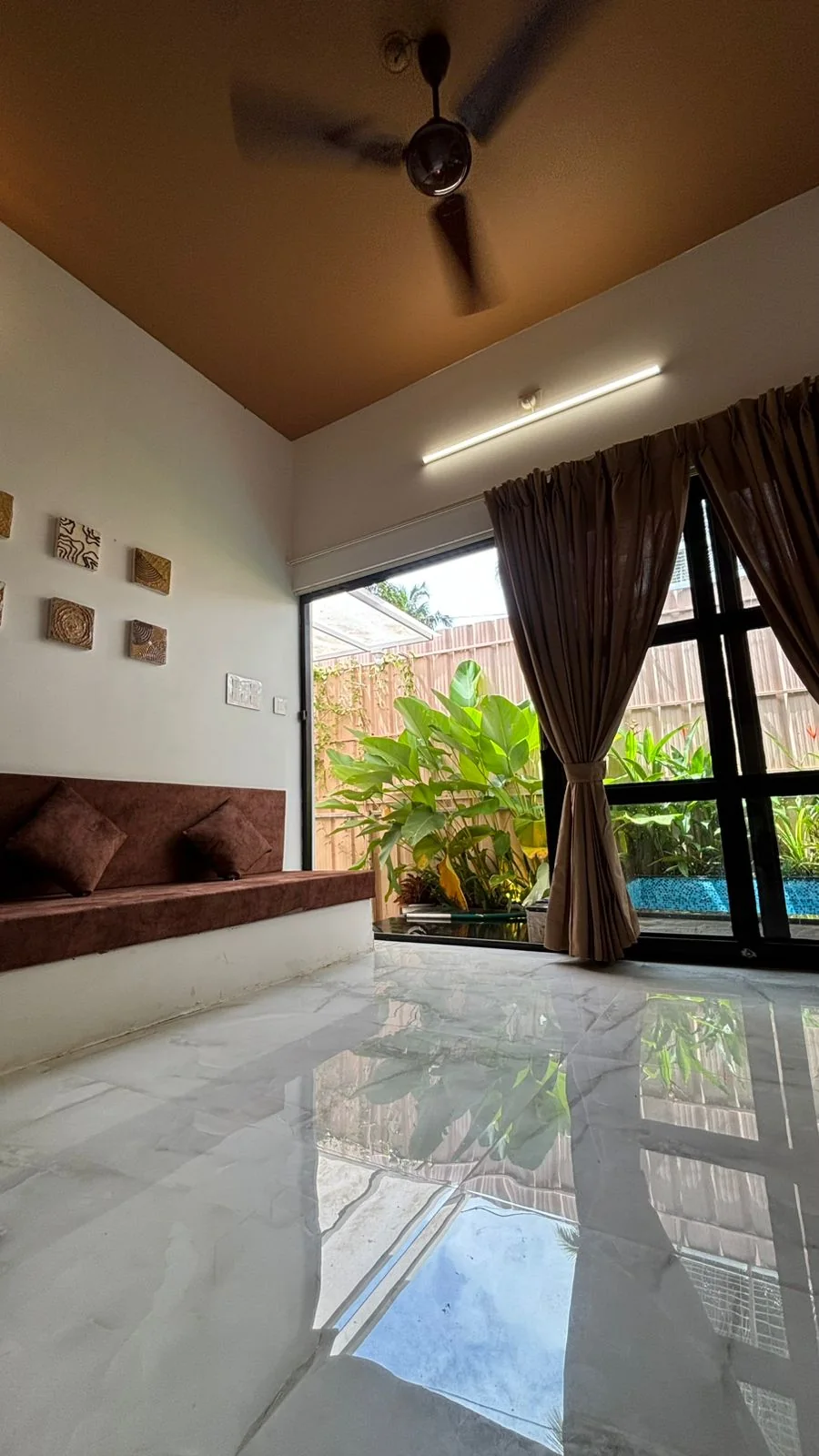 Living room with a ceiling fan, glass wall to the pool garden and a reflective marble floor