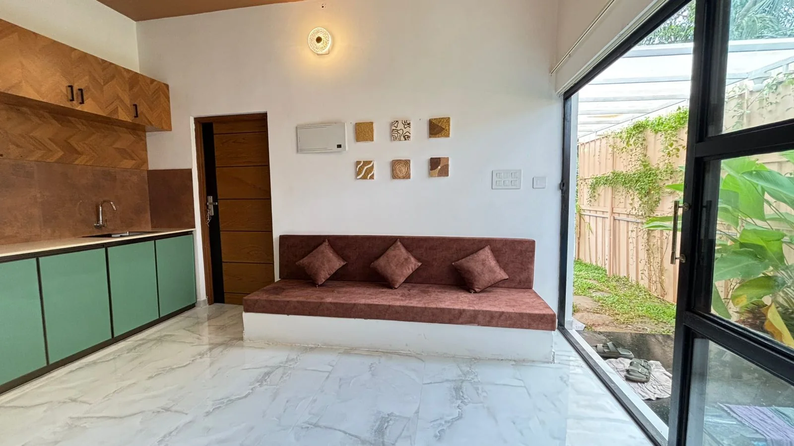 Living room with a long maroon sofa, textured wall art and a sliding glass door to the garden